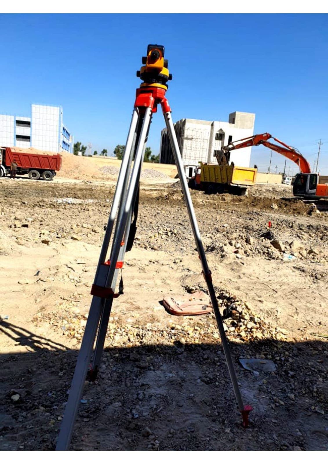 A surveying level on a tripod for setting-out, with plant and buildings behind